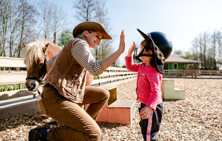 Medewerker Avonturenboerderij Molenwaard geeft highfive aan meisje